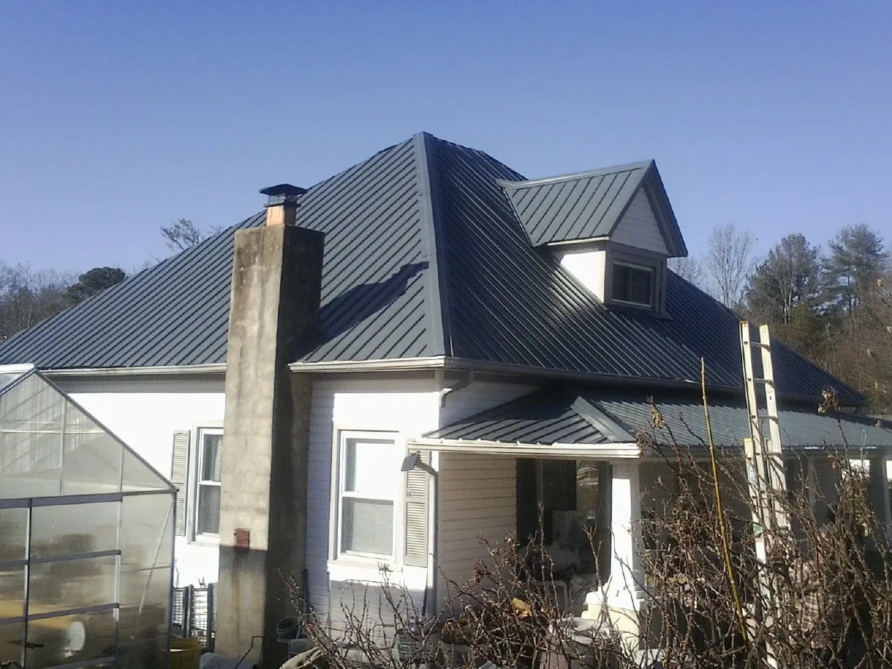 Dark blue standing seam metal roof on a white farmhouse with dormer — Slate & Tile Roof Repair by Roofing Brothers in Bardolph