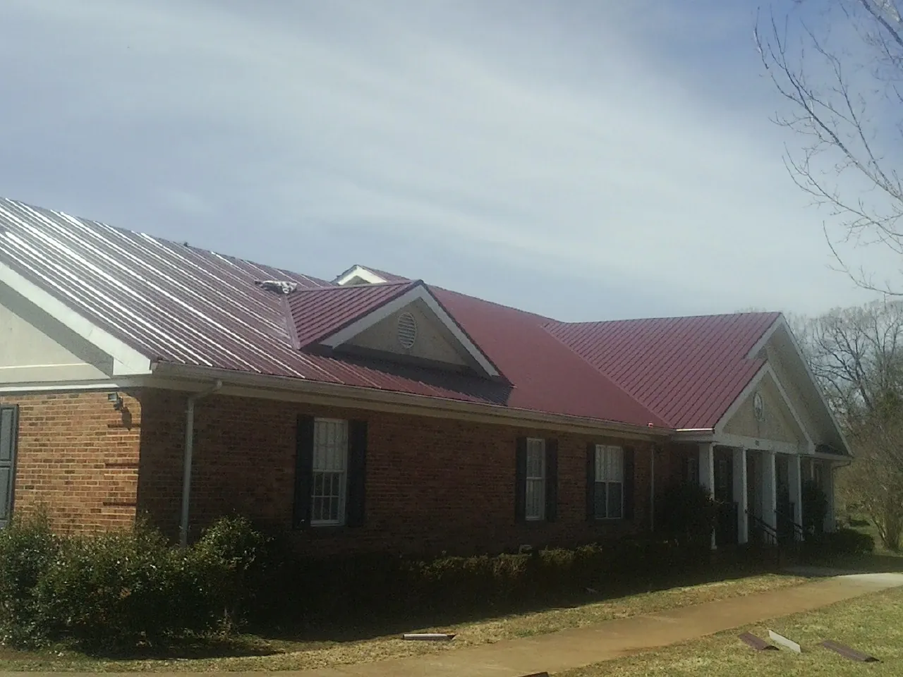 Red metal roof with gabled entries on a long brick building, from a Hail Damage Roof Repair job in Bardolph