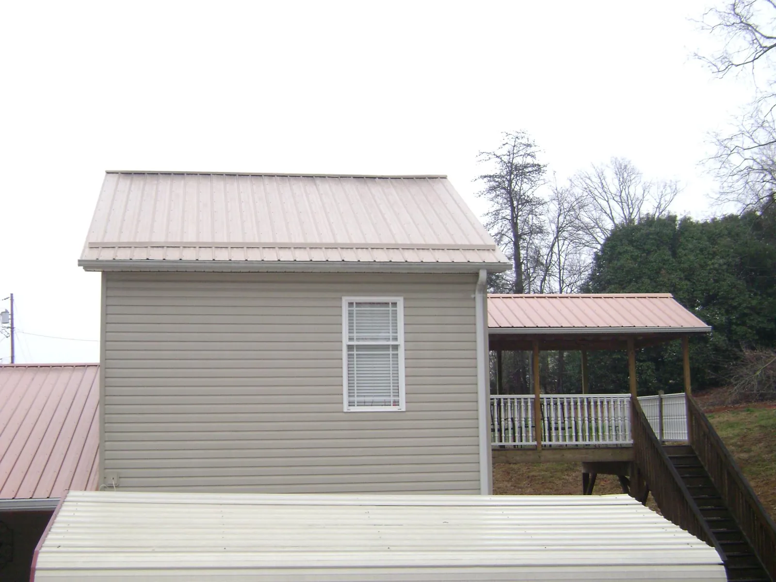 Tan metal roofs on a two story addition and attached porch, from a Roof Replacement job in Bardolph